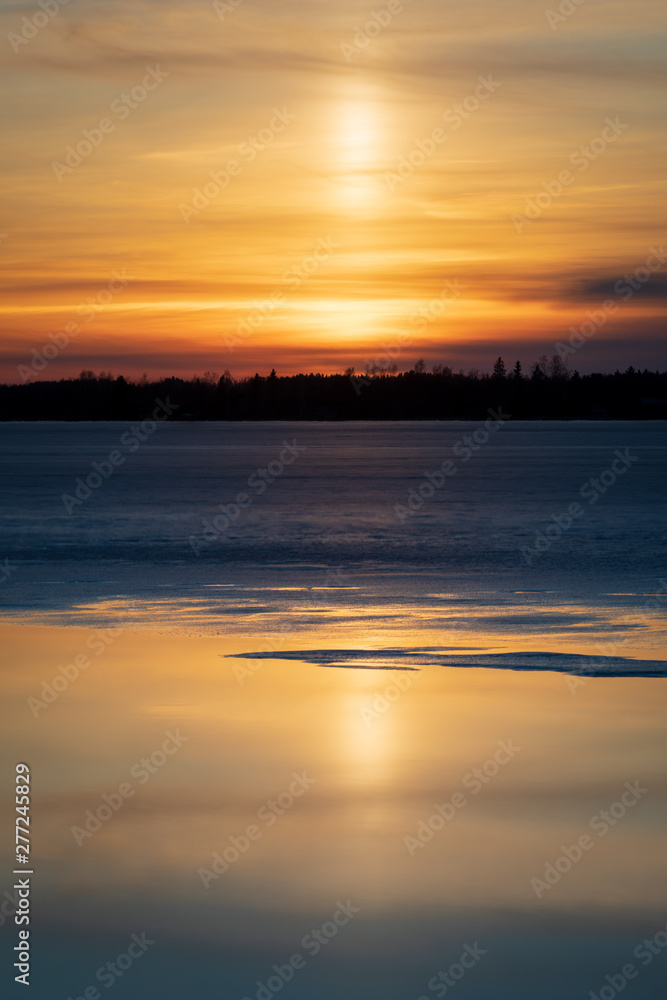 Light pillar in sunset reflecting from melting lake water