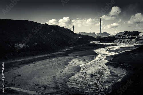 dirty river water after factory waste with piles of black waste on the background of pipes and factory workshops. Environmental disaster, black and white photo