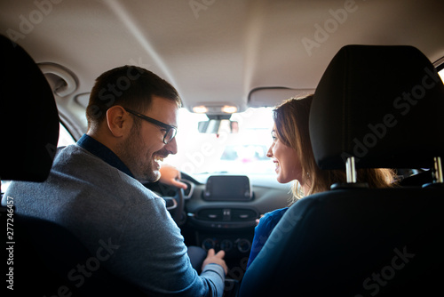 Back seat view of car interior and lovely couple sitting in front of the car looking at each other and smiling. Family buying perfect car. © littlewolf1989