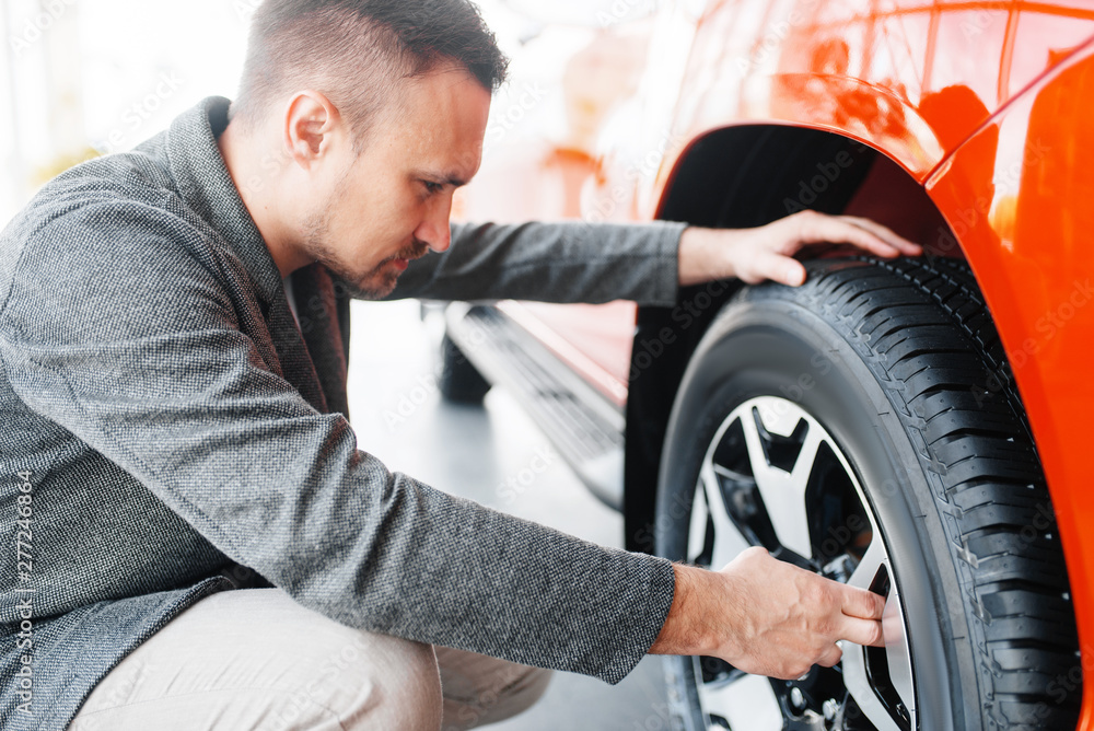 Man looks on wheels of new car in showroom Man looks on wheels of new car in showroom