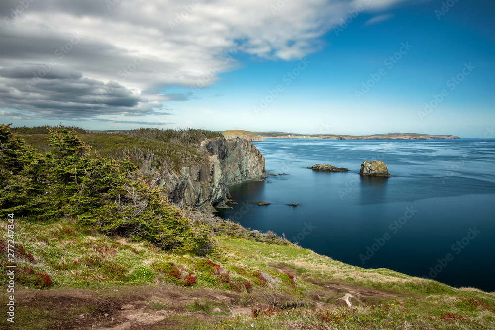 Pristine coastal seascape with soft clouds and sea stacks in beautiful clear blue water. Skerwink trail located in Port Rexton, Newfoundland Canada. 