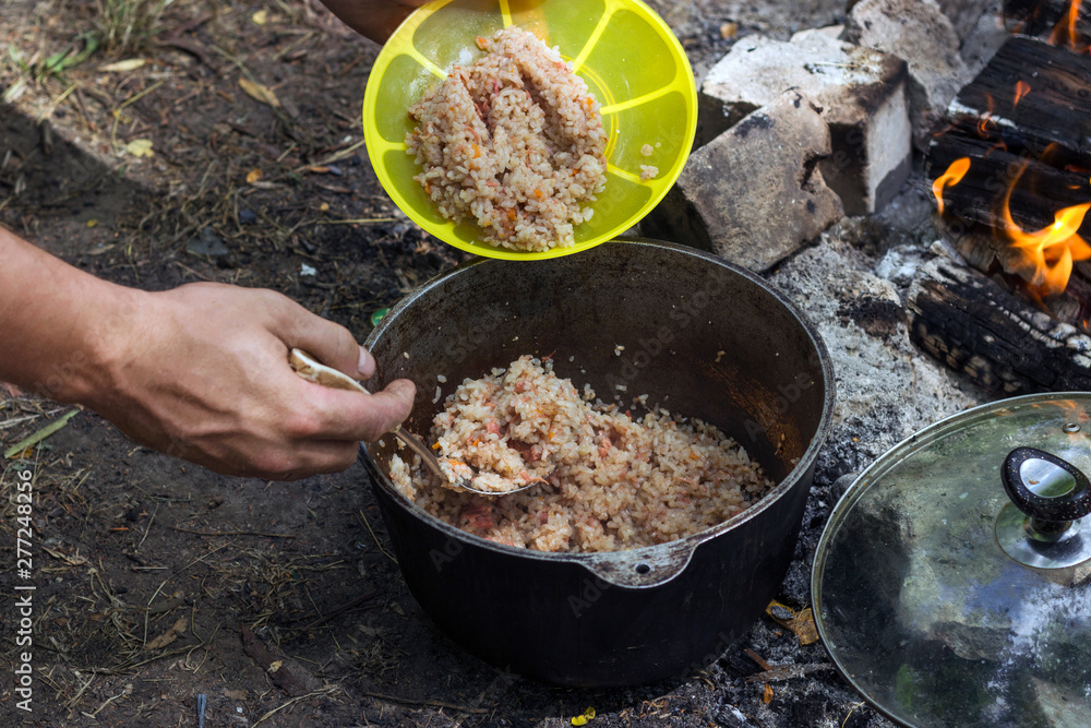 man puts porridge with meat in a bowl with a bowler hat, in nature man puts porridge with meat in a bowl with a bowler hat, in nature