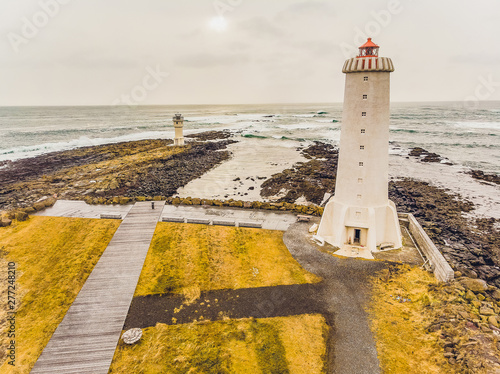 Old lighthouse White on the hill There are stone stairs around the area filled with brown hay. There is a blue sky in the background.Landscape of Iceland.