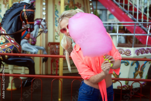 Beautiful blonde with cotton candy having fun near the carousel.