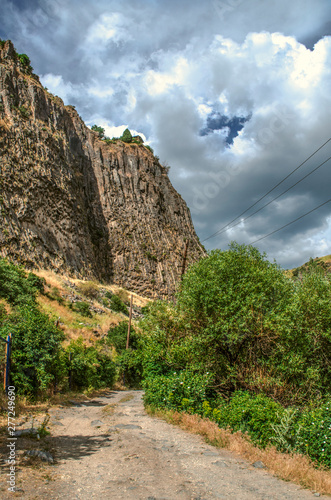 The darkened sky from the big storm clouds over the gorge Garni and the road passing about vertically standing basalt rocks and hills