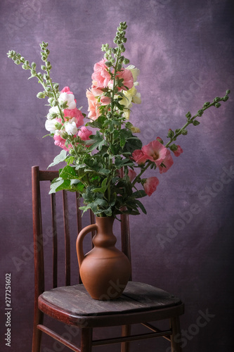 A bouquet of malva flowers in a clay vase on a chair.
