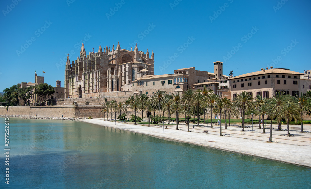 Majorca 2019: Cathedral La Seu of Palma de Mallorca on a sunny summer day with blue sky. Image composition with lake and palm trees in the foreground