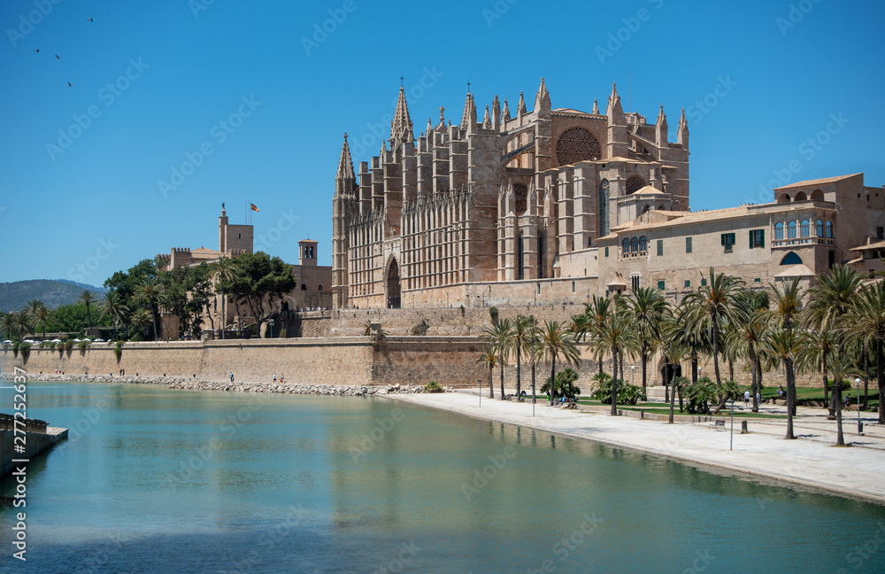 Majorca 2019: Panoramic view of Cathedral La Seu of Palma de Mallorca on a sunny summer day with blue sky. Image composition with lake and palm trees in the foreground