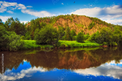 Fototapeta Naklejka Na Ścianę i Meble -  Summer landscape river with reflecting trees against the backdrop of forests and mountains.