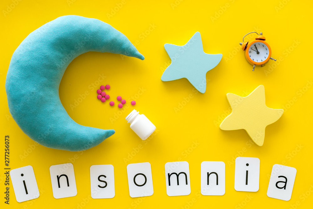 Sleeping pills near alarm clock, insomnia word and stars, moon toys on yellow background top view Sleeping pills near alarm clock, insomnia word and stars, moon toys on yellow background top view