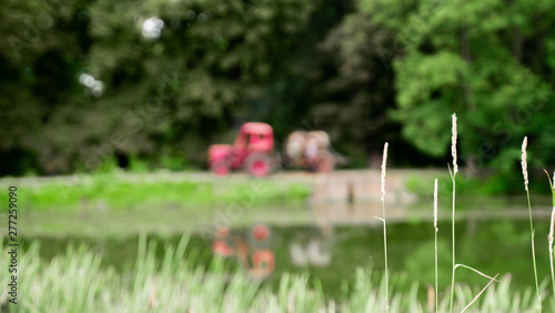 blurred forest, lake and red tractor. abstract landscape countryside background.