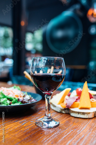 Dinner in the restaurant with Wine, Cheese and salad. Red wine glass, assorted cheese plate and smoked salmon salad on wooden dining table. This is Lunch or Dinner Restaurant or Cafe Concept Image. © Hakan Tanak
