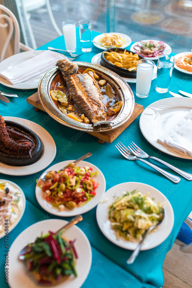 Turkish or Greek restaurant table and food dinner cuisine culture from top view. Traditional Greek ouzo or turkish raki with grilled or fried fish and appetizers on dinner table at restaurant. 
