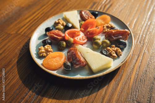 Traditional Ramadan fasting iftar snacks foods on the table. This is dates, dried apricots, black olives, tomatoes and cheese in plate on the wooden table. Snack plate.