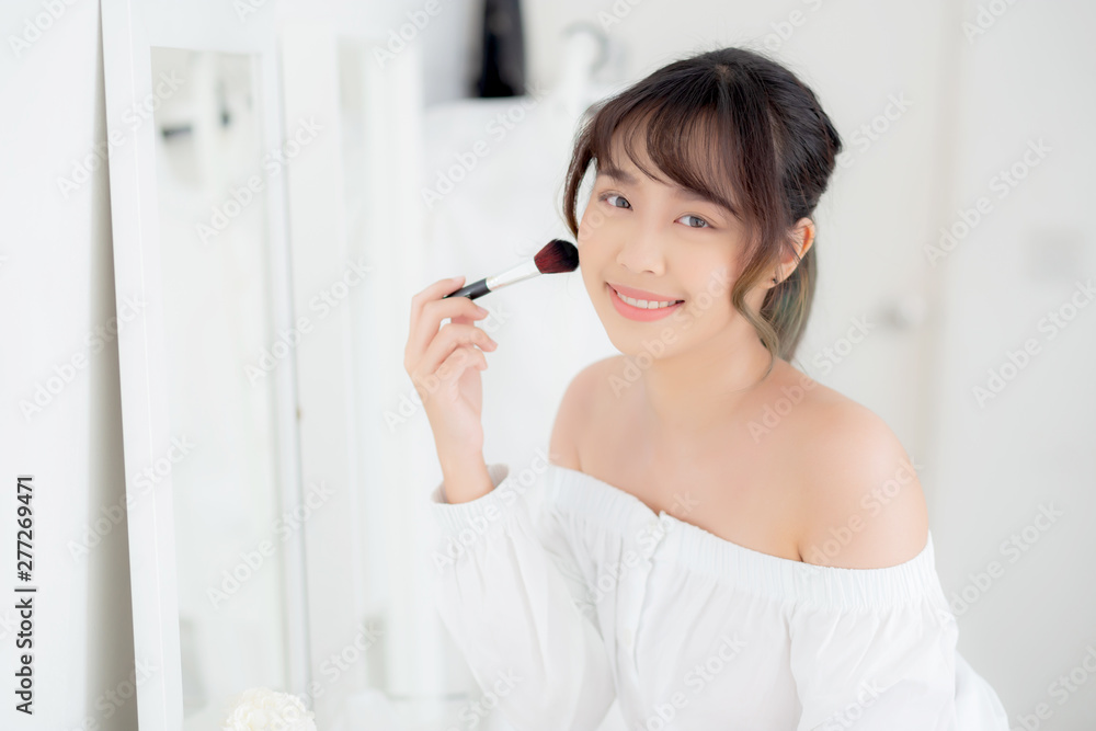 Beauty portrait young asian woman smile with face looking mirror applying makeup with brush cheek in the bedroom, beautiful of girl holding blusher, skin care and cosmetic concept. Beauty portrait young asian woman smile with face looking mirror applying makeup with brush cheek in the bedroom, beautiful of girl holding blusher, skin care and cosmetic concept.