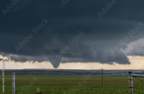 A large cone tornado under the base of a dark storm on the plains in Wyoming.