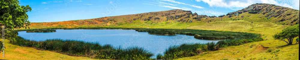 Panoramic view of the lake inside the Rano Raraku volcano crater, surrounded by lush green vegetation and under a sunny blue sky on Easter Island, Chile. Panoramic view of the lake inside the Rano Raraku volcano crater, surrounded by lush green vegetation and under a sunny blue sky on Easter Island, Chile.