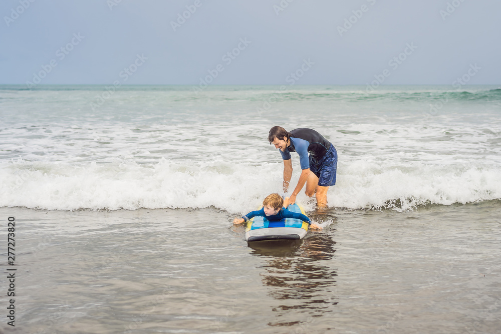 Father or instructor teaching his 5 year old son how to surf in the sea on vacation or holiday. Travel and sports with children concept. Surfing lesson for kids Father or instructor teaching his 5 year old son how to surf in the sea on vacation or holiday. Travel and sports with children concept. Surfing lesson for kids