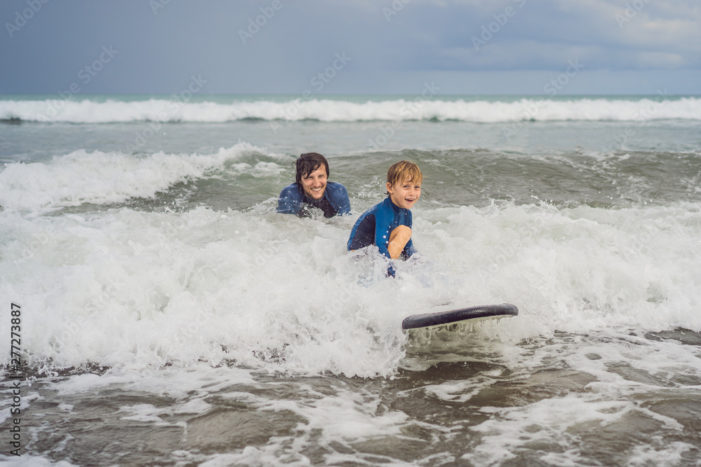 Father or instructor teaching his 5 year old son how to surf in the sea on vacation or holiday. Travel and sports with children concept. Surfing lesson for kids Father or instructor teaching his 5 year old son how to surf in the sea on vacation or holiday. Travel and sports with children concept. Surfing lesson for kids