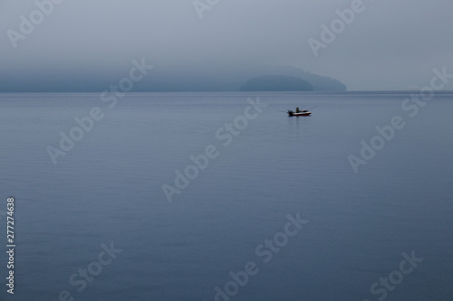 Fisherman fishing in speed boat, The boat floating in Toya Lake surrounded with fog in cloudy day at Hokkaido, Japan.