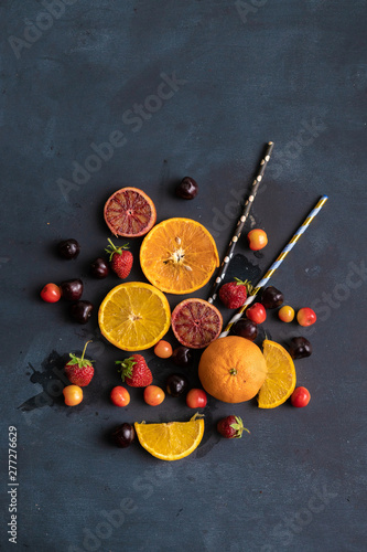 top view of glass shaped sliced fruits and berries with two tubes, juice creative concept