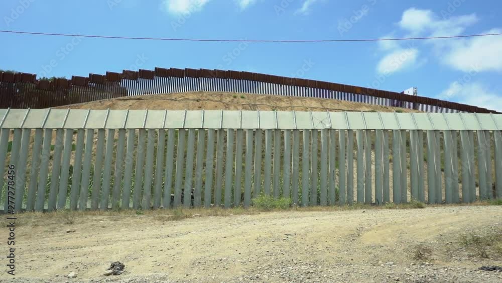Double border fence dividing USA and Mexico. Between the fence a border patrol officer can be seen driving on his ATV. Double border fence dividing USA and Mexico. Between the fence a border patrol officer can be seen driving on his ATV.