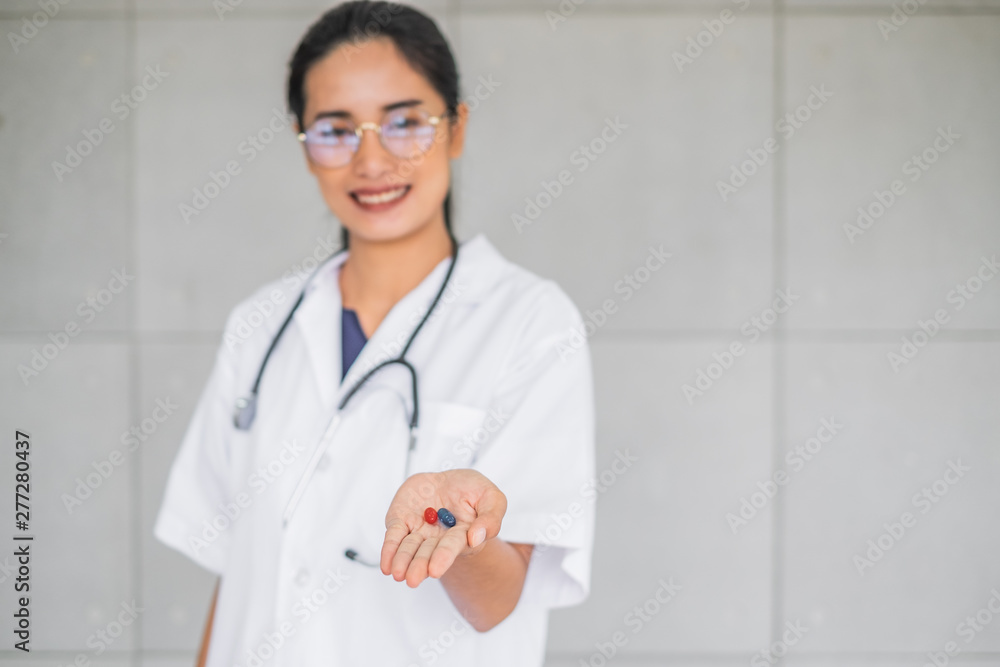 A young smiling Asian doctor holding red and blue pills in her hand. A young smiling Asian doctor holding red and blue pills in her hand.