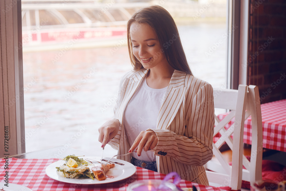 Brunette girl with long hair in a restaurant on ship on the background of the river. Girl tries salmon with rice. Girl eats appliances. The girl in the jacket after work eats. Brunette girl with long hair in a restaurant on ship on the background of the river. Girl tries salmon with rice. Girl eats appliances. The girl in the jacket after work eats.