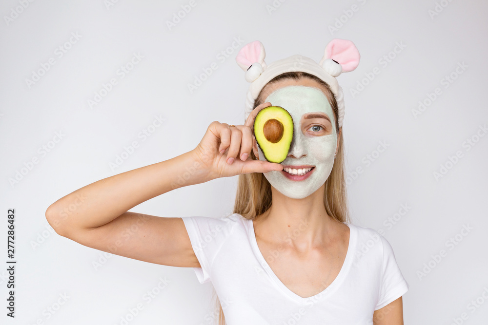 Portrait of a young woman applying natural avocado mask on her face on white background. Skin care and Spa treatments at home or beauty salon. Cosmetology concept Portrait of a young woman applying natural avocado mask on her face on white background. Skin care and Spa treatments at home or beauty salon. Cosmetology concept
