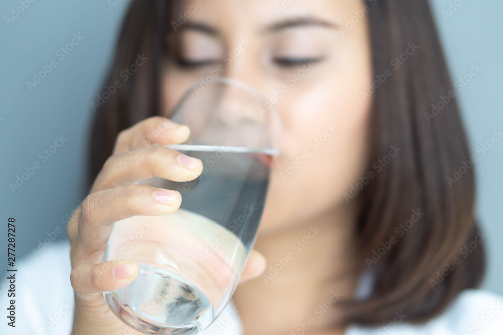 Close up woman drinking pure water from glass with blue background, Selective focus Close up woman drinking pure water from glass with blue background, Selective focus
