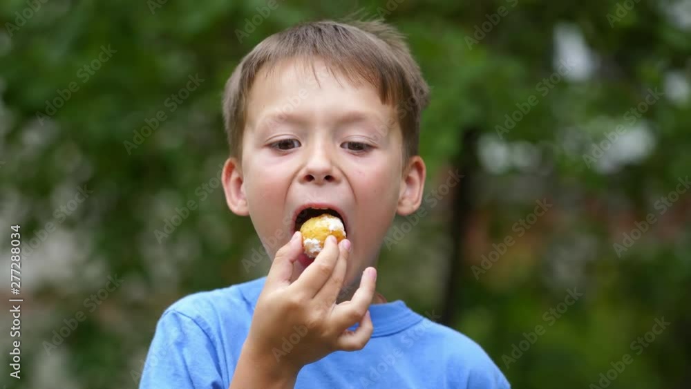 Portrait of young boy eating with mouth full outdoors. Child enjoys eating tasty donut and looking at camera in summer. Portrait of young boy eating with mouth full outdoors. Child enjoys eating tasty donut and looking at camera in summer.