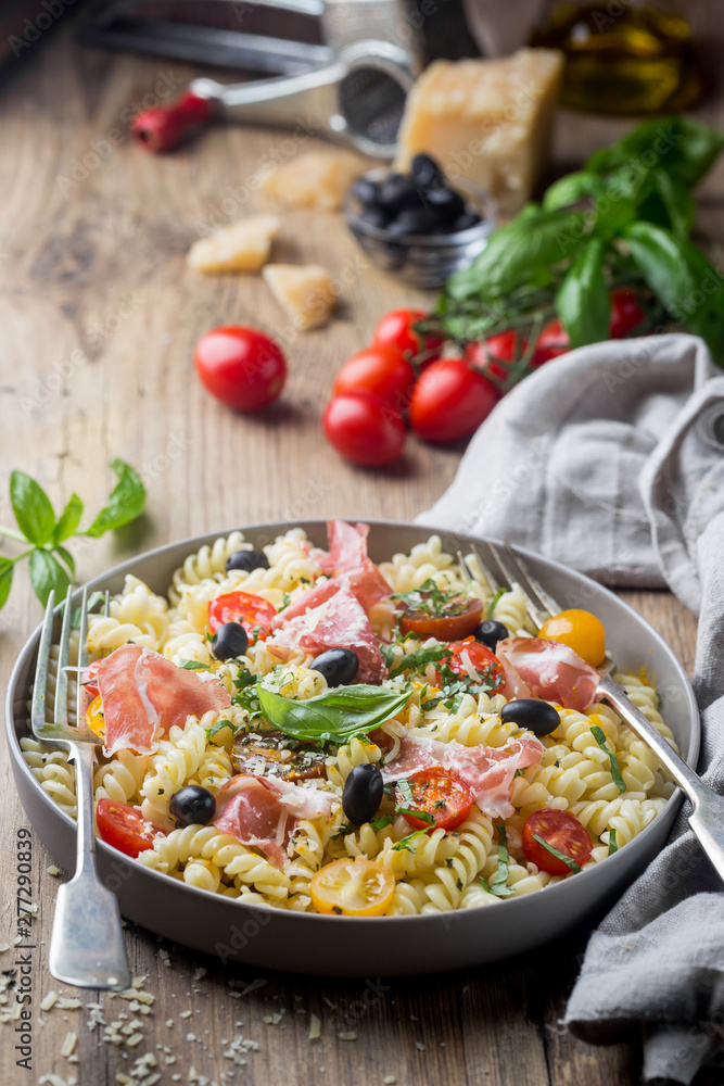 Italian fusilli spiral pasta with grape tomatoes, olives, prosciutto and parmigiano cheese on a plate Italian fusilli spiral pasta with grape tomatoes, olives, prosciutto and parmigiano cheese on a plate