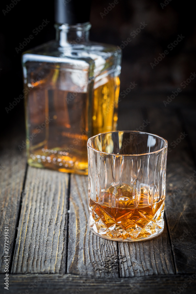 Glass and a bottle of whiskey on dark wooden table Glass and a bottle of whiskey on dark wooden table