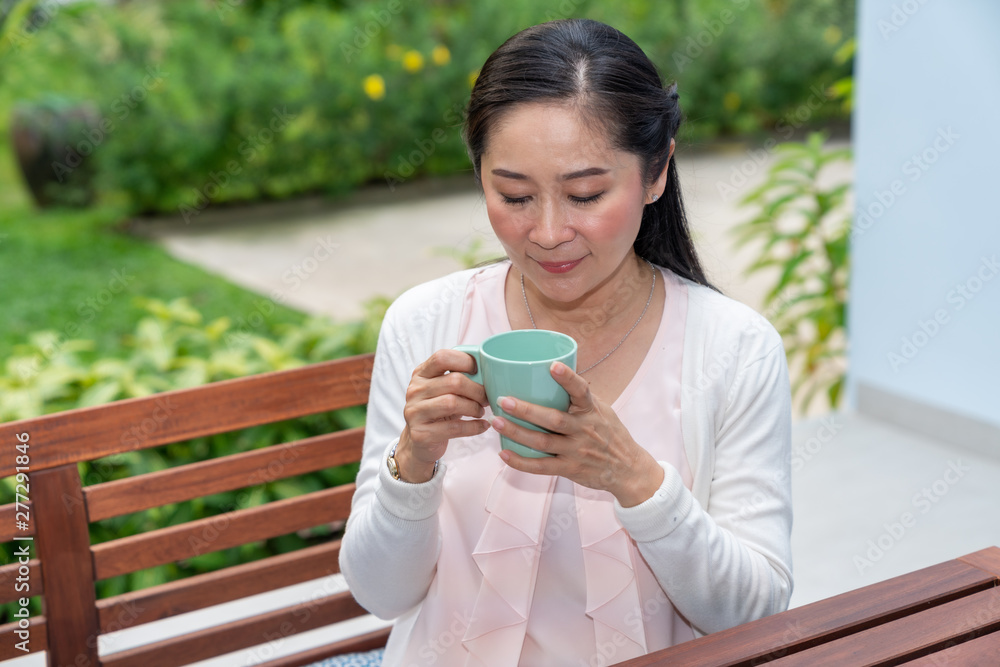 Asian woman sitting with cup of coffee at home garden Asian woman sitting with cup of coffee at home garden