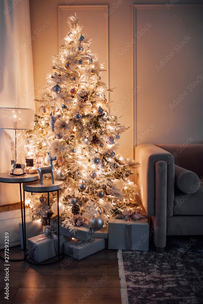 warm cozy evening in Christmas room interior design,Xmas tree decorated by lights gifts,toys, deer,candles, lanterns, garland lighting indoors fireplace.holiday.magic New year