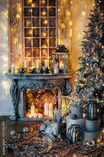 warm cozy evening in Christmas room interior design,Xmas tree decorated by lights gifts,toys, deer,candles, lanterns, garland lighting indoors fireplace.holiday.magic New year