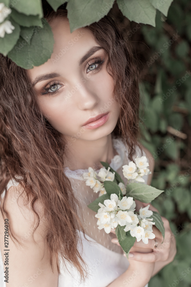 beautiful cute tender girl with dark hair in a white summer dress with a jasmine flower in hands beautiful cute tender girl with dark hair in a white summer dress with a jasmine flower in hands