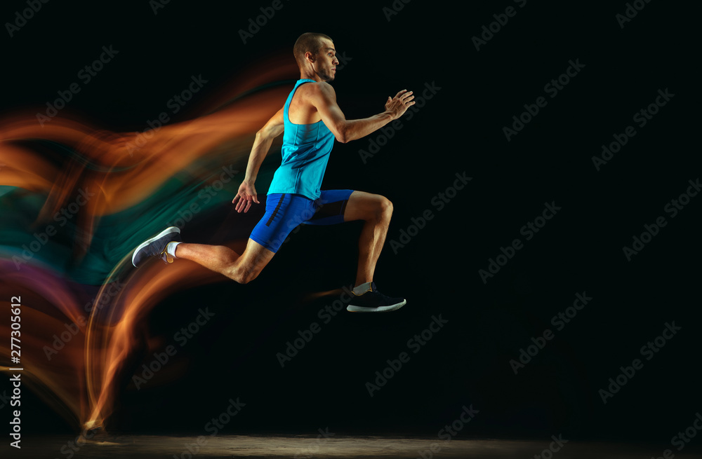 Professional male runner training isolated on black studio background in mixed light. Man in sportsuit practicing in run or jogging. Healthy lifestyle, sport, workout, motion and action concept. Professional male runner training isolated on black studio background in mixed light. Man in sportsuit practicing in run or jogging. Healthy lifestyle, sport, workout, motion and action concept.