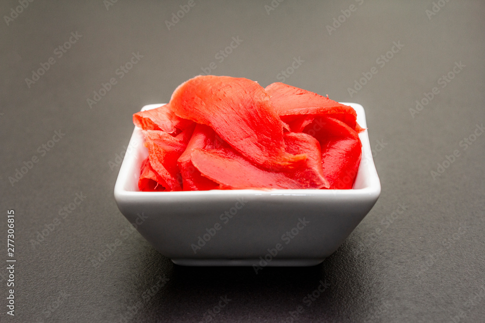 Pickled sushi ginger slices in white bowl on stone background Pickled sushi ginger slices in white bowl on stone background