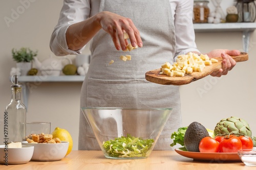 Cooking. A chef pours mozzarella or feta cheese, in the process of a vegetarian salad in the home kitchen. Light background. Restaurant menu, menu, recipe book. Healthy nutrition, detox