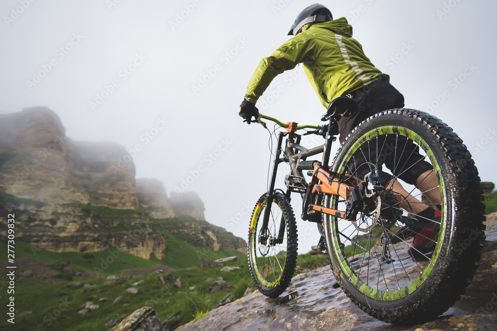 Rear view wide angle of a man on a mountain bike stands on a rocky terrain and looks at a rock. The concept of a mountain bike and mtb downhill