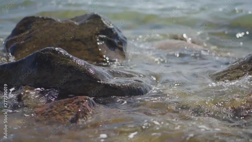 Slow Motion, waves splashing over rocks and wash around them on a sunny day Slow Motion, waves splashing over rocks and wash around them on a sunny day