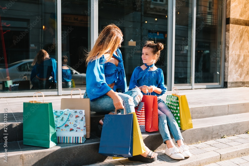 sale, consumerism and people concept - happy young women her dauther with shopping bags walking city street