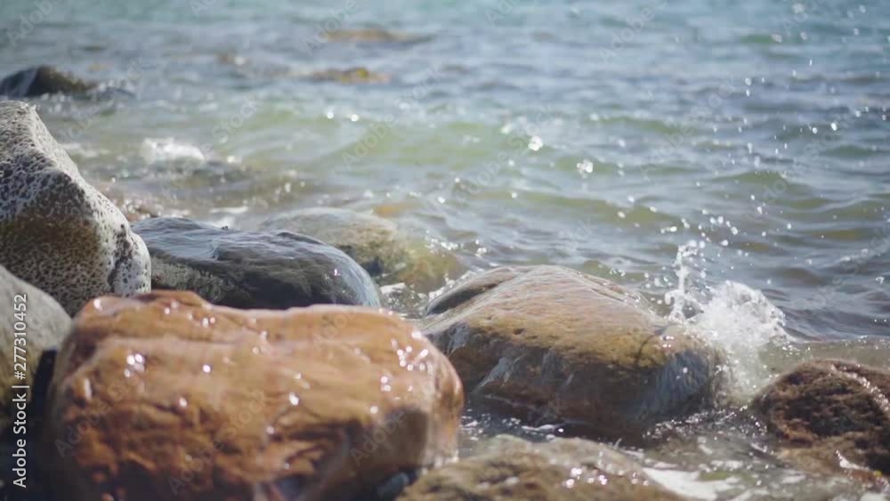Slow Motion, waves splashing over rocks and wash around them on a sunny day Slow Motion, waves splashing over rocks and wash around them on a sunny day