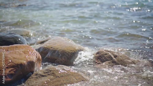 Slow Motion, waves splashing over rocks and wash around them on a sunny day