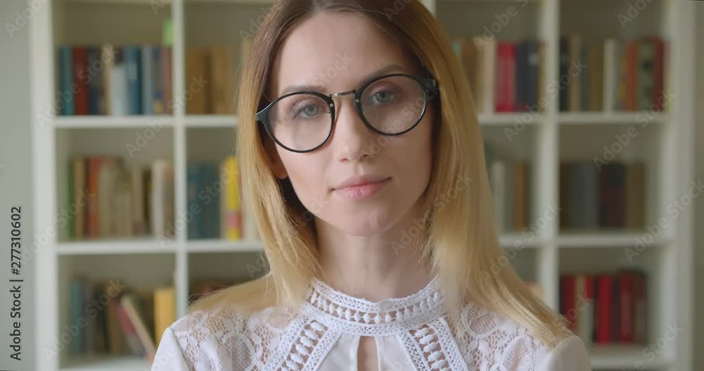 Closeup portrait of young pretty caucasian female student in glasses smiling cheerfully looking at camera in the college library Closeup portrait of young pretty caucasian female student in glasses smiling cheerfully looking at camera in the college library