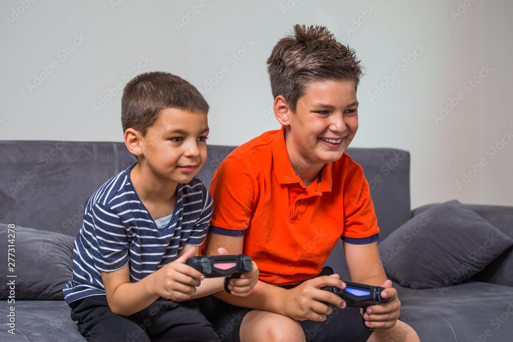 Two kids playing on the console sitting on the couch. Cheerful kids are  sitting together on sofa at home playing video games Stock-foto | Adobe  Stock