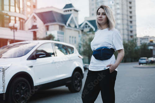 Young business woman with blue belt denim bag on it standing at the street on high heels near the white car © zalesky