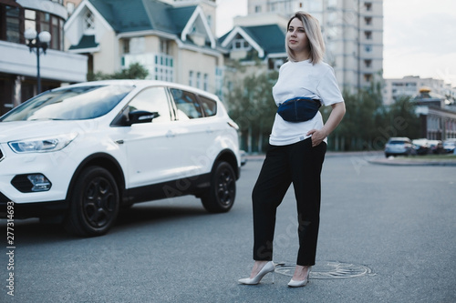 Young business woman with blue belt denim bag on it standing at the street on high heels near the white car © zalesky