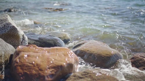 Slow Motion, waves splashing over rocks and wash around them on a sunny day